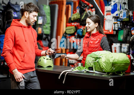 L'achat d'équipement sportif l'homme à l'aide de smart phone à la caisse avec vendeuse dans la boutique avec les articles de voyage Banque D'Images