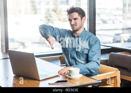 N'aiment pas ! Vue latérale de la critique négative portrait jeune barbu freelancer dans blue jeans chemise sont assis dans un café et faire appel vidéo sur ordinateur portable et Banque D'Images