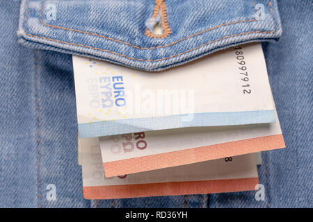 Veste jeans classique usé poche avant avec peu de monnaie euro billets en papier. Les petits gains ou de l'argent de poche. Symbole de la pauvreté et de la crise financière. Fermer- Banque D'Images
