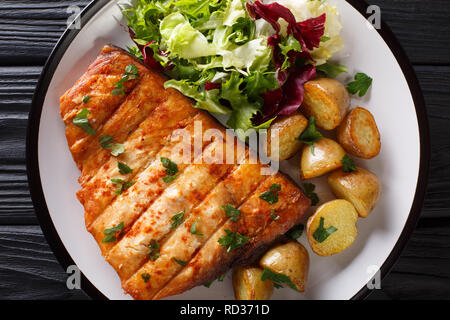 Steak d'espadon frit avec bébé pommes de terre et salade fraîche close-up sur une plaque sur une table en bois. haut horizontale Vue de dessus Banque D'Images