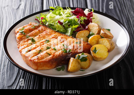 Grill steak servi d'espadon et pommes de terre salade fraîche close-up sur une plaque sur un fond noir. Banque D'Images