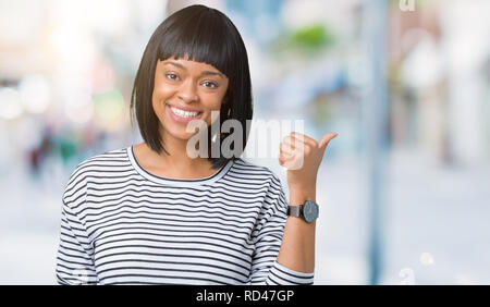 Beau young african american woman wearing sweater à rayures sur fond isolé avec sourire heureux face à la recherche et en pointant sur le côté avec Banque D'Images