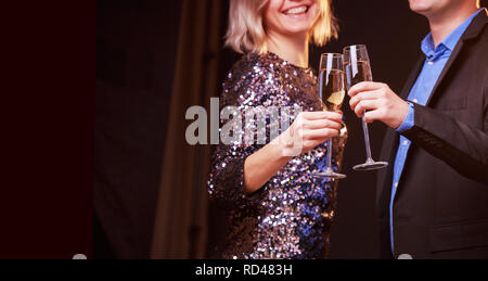 Photo de femme en robe brillante et les hommes avec des verres à vin avec champagne sur fond noir Banque D'Images