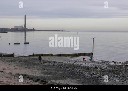 Carrickfergus, comté d'Antrim, Irlande du Nord. 17 janvier 2019. Météo au Royaume-Uni - nuage gris sur Carrickfergus lors d'une journée froide mais calme sur Belfast Lough. Parents et enfants jouant sur le rivage à Carrickfergus avec Kilroot Power Station en arrière-plan. Crédit : David Hunter/Alay Live News. Banque D'Images