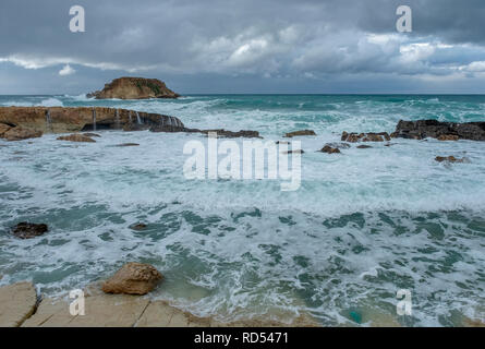 Mer grosse batter le littoral de la côte d'Agios Georgios à Chypre, avec la petite île de Yeronisos derrière. Banque D'Images