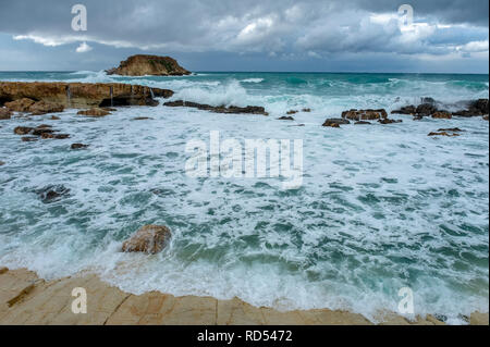 Mer grosse batter le littoral de la côte d'Agios Georgios à Chypre, avec la petite île de Yeronisos derrière. Banque D'Images