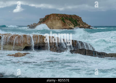 Mer grosse batter le littoral de la côte d'Agios Georgios à Chypre, avec la petite île de Yeronisos derrière. Banque D'Images