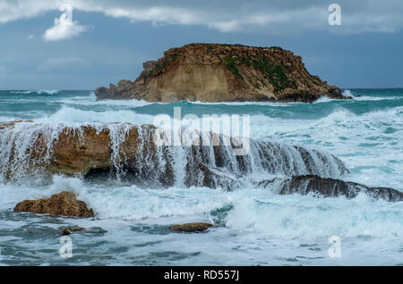 Mer grosse batter le littoral de la côte d'Agios Georgios à Chypre, avec la petite île de Yeronisos derrière. Banque D'Images