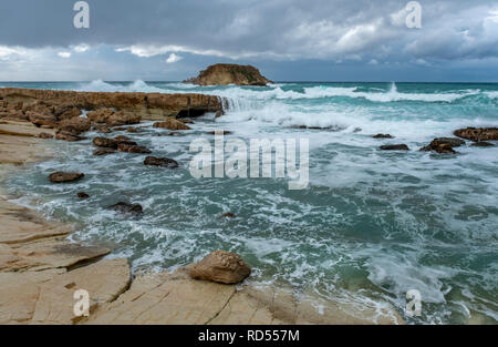 Mer grosse batter le littoral de la côte d'Agios Georgios à Chypre, avec la petite île de Yeronisos derrière. Banque D'Images