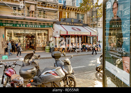 Des scooters garés dans une rue de Paris à côté d'un panneau publicitaire avec les gens assis dehors en train de déjeuner au café de la Comédie, rue Saint Honoré, Paris Banque D'Images