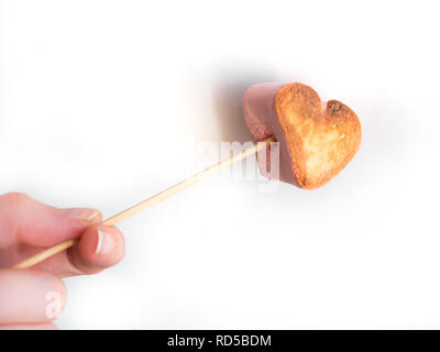 Forme coeur grillé sur une brochette de guimauves dans femme Main sur fond blanc. Banque D'Images