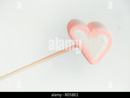 Sur une brochette de guimauve rose close up fond blanc, un coeur des guimauves sur un bâton prêt à fry, bonbons en forme de cœur de guimauve. V Banque D'Images