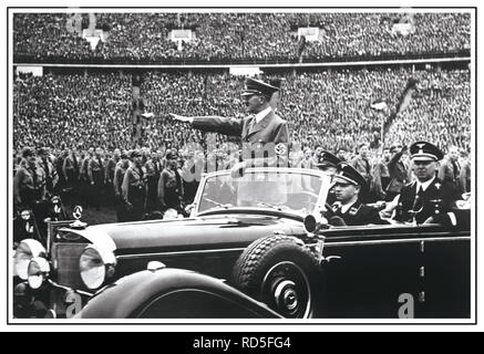 Adolf Hitler en uniforme portant un brassard à croix gammée Heil Hitler donne hommage à l'armée et de la foule à un immense rassemblement nazis en 1938 en Allemagne. Hitler salue les participants à un Reichsparteitag (Reich Partie jour) à Nuremberg, Allemagne. Martin Bormann en uniforme assis également présent dans l'arrière de la voiture Mercedes à toit ouvert Banque D'Images