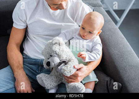 Adorable bébé fille jouer avec ours assis avec le père sur la table à la maison Banque D'Images