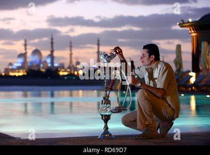 Homme avec narguilé, pipe à eau, piscine de l'hôtel, le Shangri-La Hotel, Qaryat Al Beri, vue sur la Mosquée Sheikh Zayed, Abu Dhabi Banque D'Images