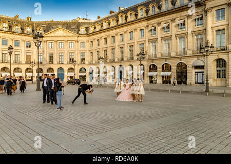 Un photographe prend une photo d'une jeune mariée chinoise dans sa robe de mariage avec ses demoiselles d'honneur à ses côtés à la Place Vendôme , Paris, France Banque D'Images