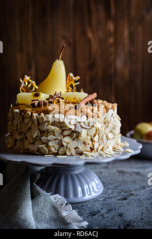 Délicieux gâteau en couches avec glaçage au caramel, décoré avec des tranches de poires, d'amandes, sucre filé décorations et des bâtons de cannelle Banque D'Images