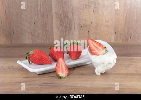 Fondu à la crème fouettée avec des fraises sur une assiette blanche et un fond de bois -imagen Banque D'Images