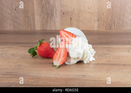 Fondu à la crème fouettée avec des fraises sur une assiette blanche et un fond de bois -imagen Banque D'Images