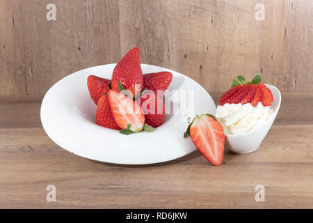 Fraises et crème fouettée sur une assiette blanche sur un fond de bois. - Imagen Banque D'Images