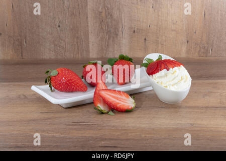 Fraises et crème fouettée sur une assiette blanche sur un fond de bois. - Imagen Banque D'Images