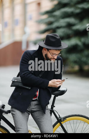 Hipster barbu beau man using a smart phone et smiling while riding bicycle in city Banque D'Images