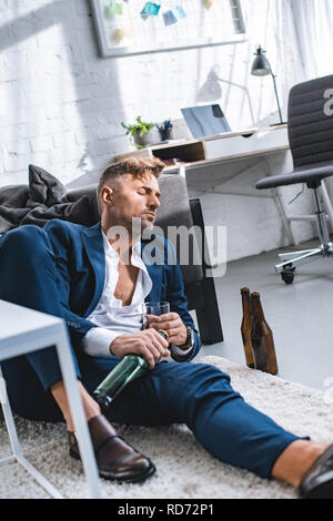 Drunk businessman assis sur un tapis avec les yeux fermés Banque D'Images