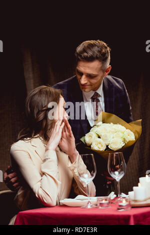 Présentation de l'homme surpris à fleurs femme pendant date romantique au restaurant Banque D'Images