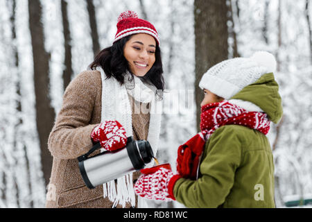 African American mother smiling et verser le thé de thermos en rouge support de cuvette par fille dans winter park Banque D'Images