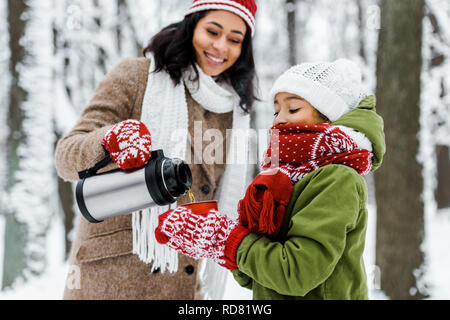 African American Woman smiling attractive et verser le thé de thermos en rouge support de cuvette par fille dans winter park Banque D'Images