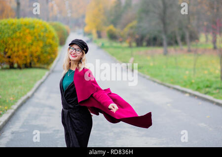 Jolie jeune femme dans les verres et les PAC, dans un manteau rouge marche dans le parc à l'automne de l'année Banque D'Images