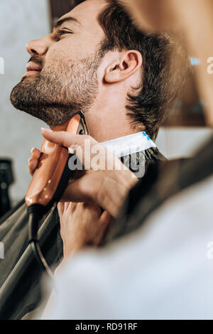 Close-up vue partielle de l'aide de coiffure et de coupe tondeuse à barbe client en instituts de beauté Banque D'Images