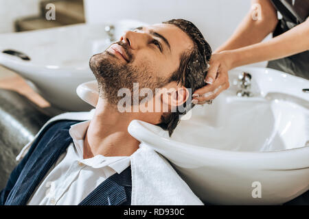 Vue partielle de l'hairstylist lavage des cheveux à handsome smiling man en instituts de beauté Banque D'Images