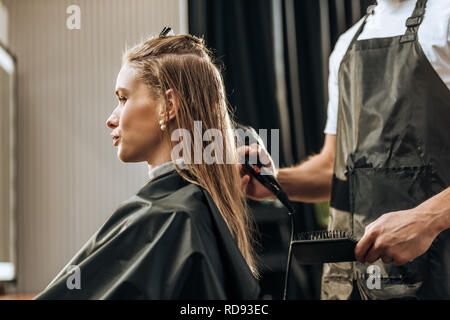 Cropped shot of hairdresser holding hairbrush et sécher les cheveux pour jolie jeune fille en instituts de beauté Banque D'Images