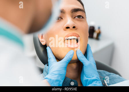 Selective focus masculins les mains dans des gants en latex toucher face de handsome african american man avec la bouche ouverte Banque D'Images