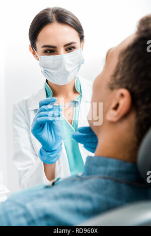 Portrait de femme stomatologist gants en latex et masque l'examen des patients afro-américains Banque D'Images