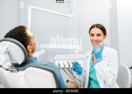 Cheerful dentiste holding drill et souriant près de african american patient Banque D'Images