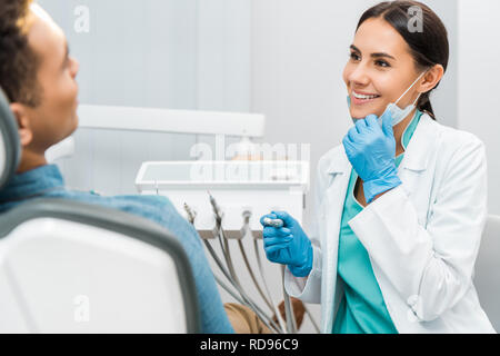 Cheerful female dentist holding mask et percer et près du patient smiling Banque D'Images