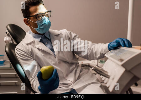 African American dentiste dans lunettes et masque holding apple Banque D'Images