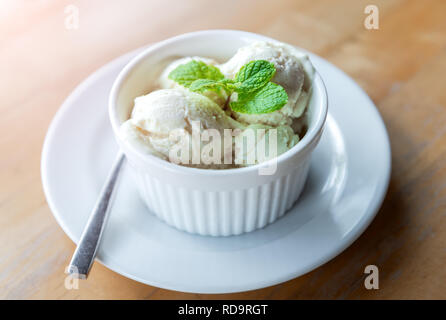 Vanille lait glaces avec feuille de menthe en blanc tasse matin avec un éclairage chaleureux. Banque D'Images