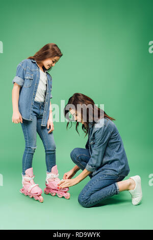 Mère en mettant en denim sur rollers fille sur fond vert Banque D'Images