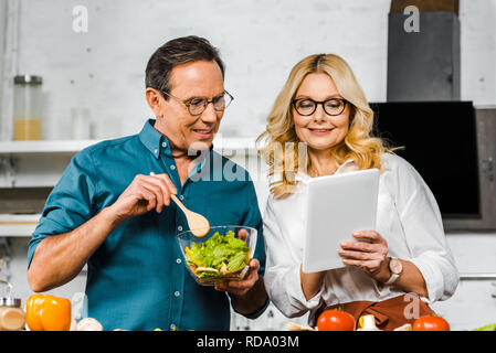 Femme mature montrant quelque chose sur la tablette au mari dans la cuisine Banque D'Images