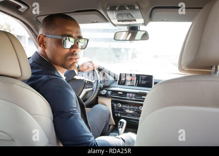 Jeune gardien de sécurité conducteur en voiture lunettes assis à l'intérieur à la caméra arrière siège arrière graves voir Banque D'Images