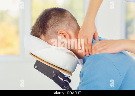 Le massage sur chaise de massage dans le bureau. Masseur massage n à un homme assis sur un fauteuil de massage dans une clinique. Banque D'Images