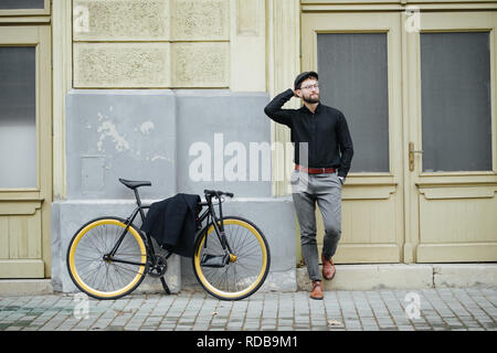 Homme barbu hippie chic dans la street bike sac à main en cuir, lunettes. La photographie de style vintage, des effets de lumière. Vieille ville européenne Banque D'Images