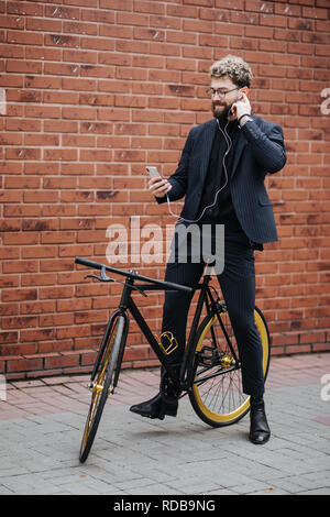 L'homme d'affaires barbu beau écouter de la musique en ville en vélo. Banque D'Images