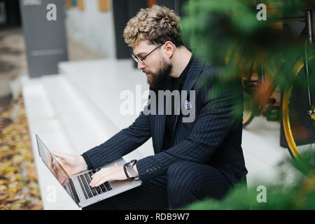 Portrait de jeune homme barbu beau côté à l'aide d'ordinateur portable avec location à l'extérieur. Banque D'Images