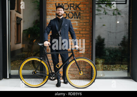 Le mode de vie, de transport et de personnes concept. Jeune homme à lunettes riding bicycle on city street sur brickwall Banque D'Images