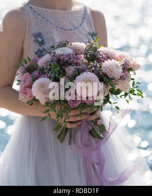 La mariée tient un bouquet de mariage rose et lilas dans ses bras contre le fond de la mer Banque D'Images