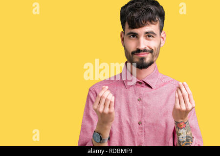 Beau jeune homme portant chemise rose sur fond isolé faisant le geste avec la main d'argent, demande de paiement de salaires, d'affaires millionnaire Banque D'Images